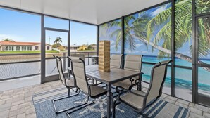 A covered outdoor seating area with a view of the ocean and palm trees.