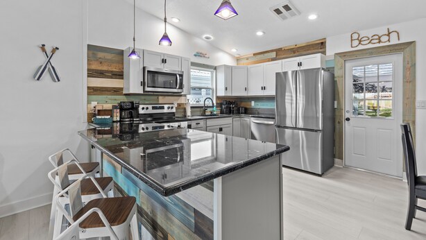 A modern kitchen with a central island, stainless steel appliances, pendant lighting, and a view of the outdoors.