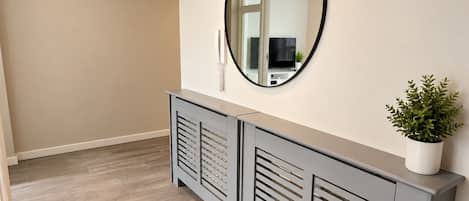 A hallway with a grey console table, a round mirror, and a potted plant.