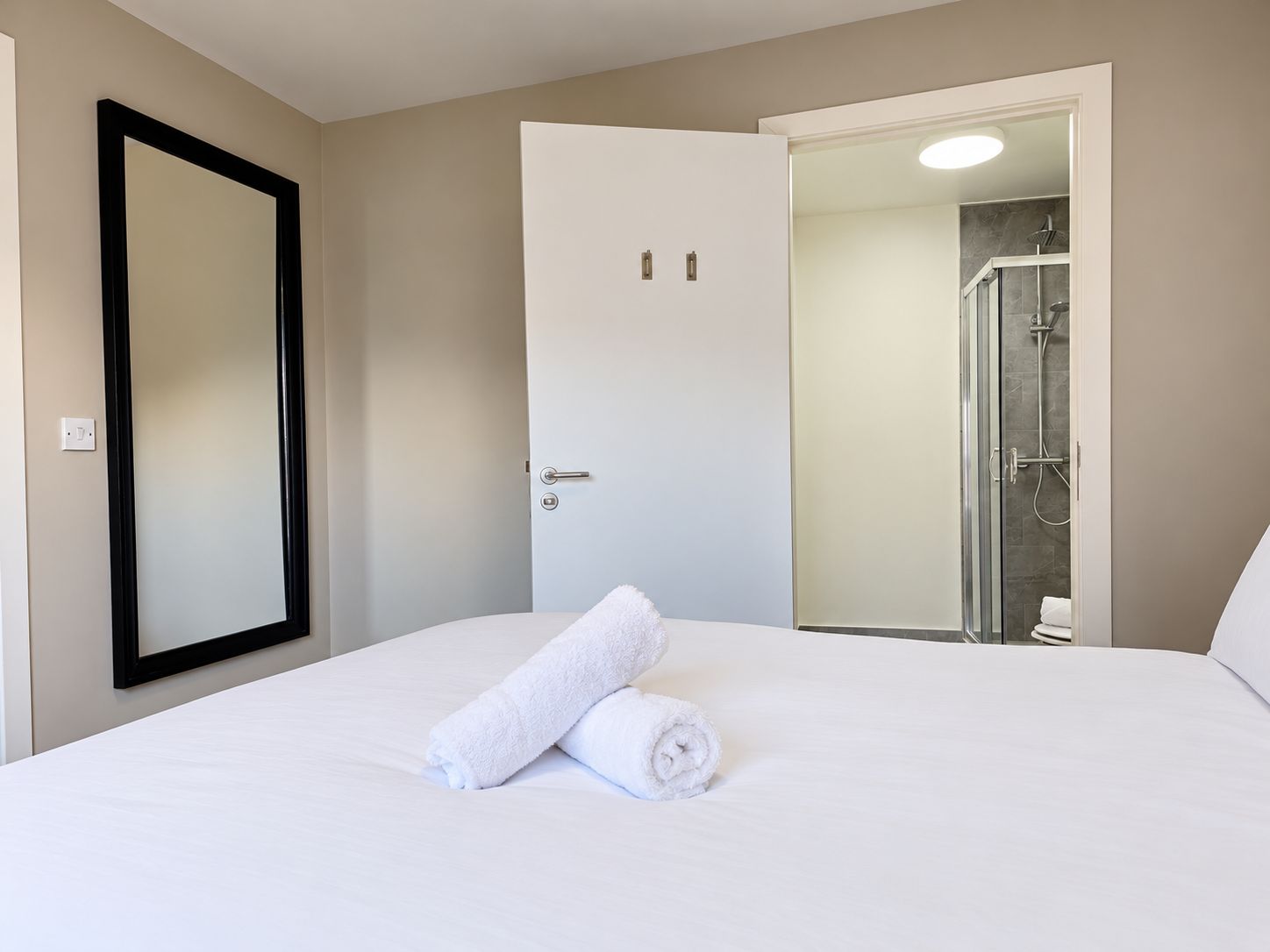 A hotel room with a bed, a door, and a shower area.