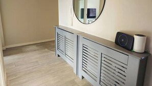 Una habitación moderna con una mesita consola gris, un espejo redondo y un objeto cilíndrico blanco encima.