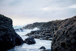 A rocky coastal landscape with large boulders and waves crashing against them.