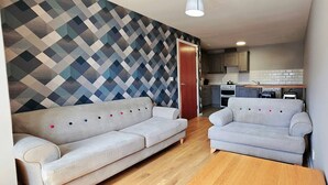 A living room with two sofas, a wooden floor, and a kitchen in the background. - Central Apartment in Belfast City Centre (Belfast)
