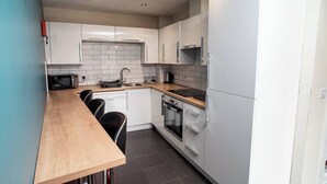 Ett kompakt kök med vita skåp, en träbänkskiva, en inbyggd ugn och en diskmaskin.