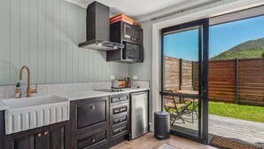 A modern kitchen with dark cabinetry, a stainless steel refrigerator, and a large window overlooking a wooden deck.