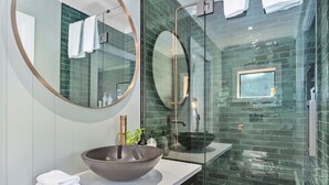 A modern bathroom with a large round mirror, a vessel sink, and a glass-enclosed shower area.