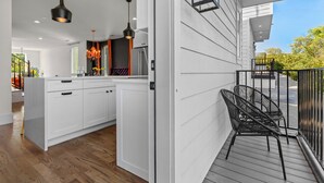 A modern kitchen with white cabinets, a wooden floor, and a balcony with a black chair.