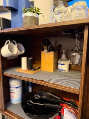 A shelf with a potted plant, white mugs, a wine glass, a knife block, and a canister.