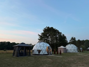 Three geodesic dome structures in an open field with a clear sky.