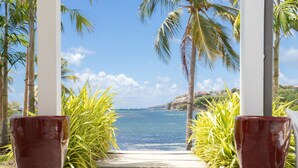 Vista desde una veranda con océano despejado y palmeras, que conduce a una playa.