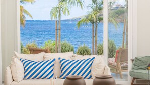 Una habitación con vistas al mar, un sofá con almohadones a rayas, una silla de mimbre y una silla verde.