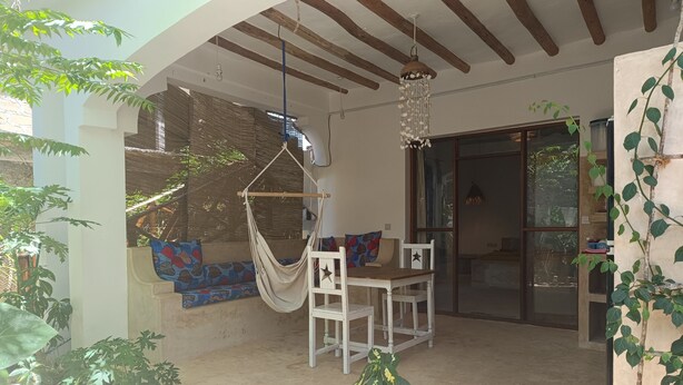 Un patio con una hamaca, una mesa de madera y sillas. Se ve una ventana con vistas al exterior.