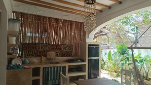 Una cocina con vigas de madera, una lámpara colgante, un refrigerador y una ventana con vistas a la vegetación.