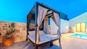A modern outdoor bedroom with a canopy bed, stone wall, and a swimming pool. - Amazing home in Zagrad (Zagrad)