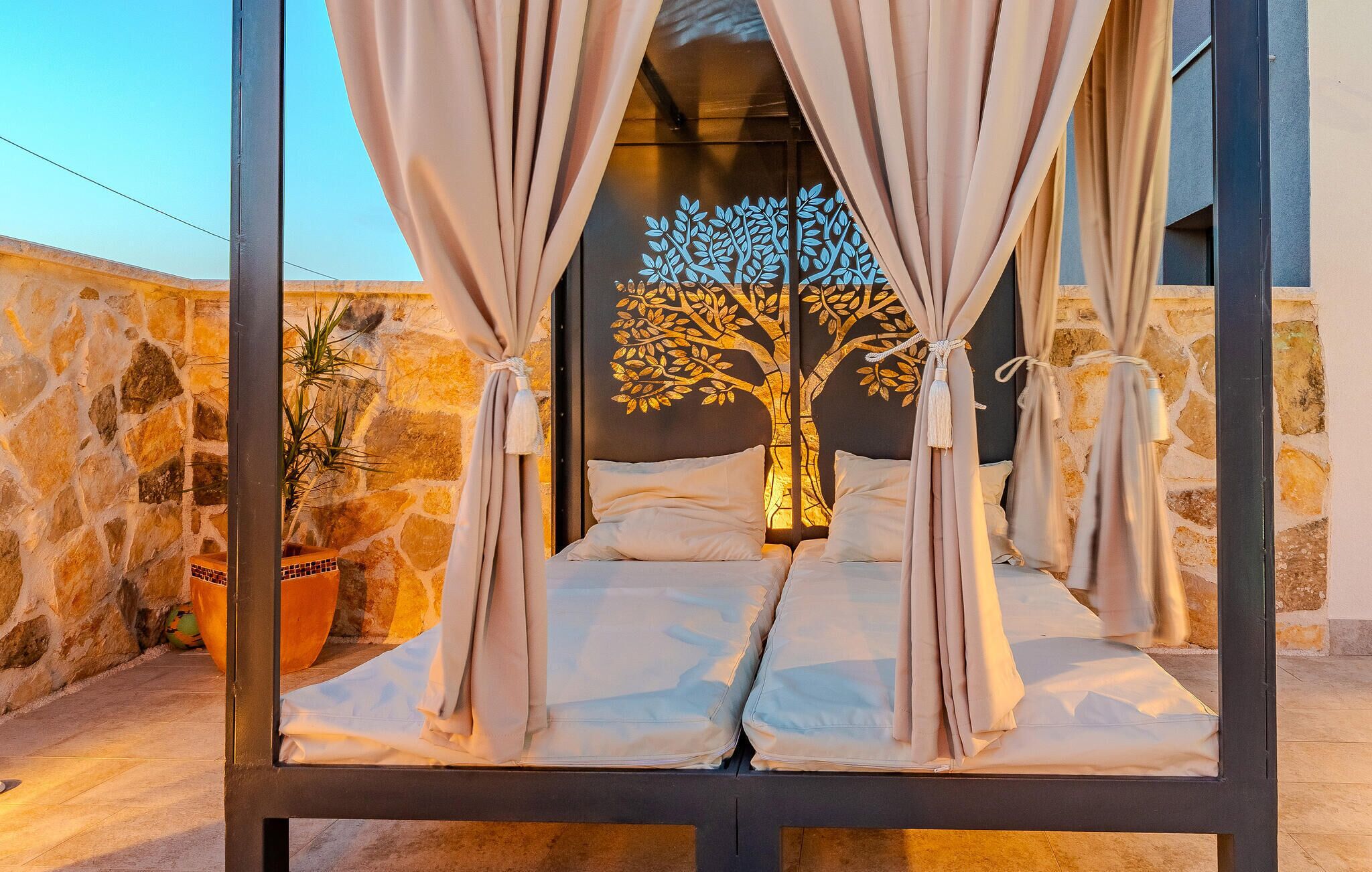 A bed with beige curtains and a tree mural on the wall behind it.