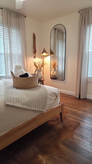 Une chambre à coucher avec un lit en bois, une lampe de chevet, un miroir et un panier en osier posé sur le lit.