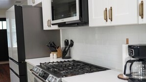 A modern kitchen with white cabinets, a black refrigerator, a microwave, a stove, and a coffee maker.