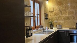 Une cuisine avec des murs en pierre, une fenêtre avec des volets en bois, un évier et une cuisinière.
