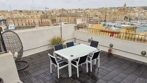 Une terrasse sur le toit, avec une table et des chaises blanches, un barbecue en métal et une vue sur une marina remplie de bateaux.