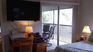 Ein Hotelzimmer mit Bett, Schreibtisch mit Stuhl, Fernseher und Balkon mit Sitzgelegenheit.