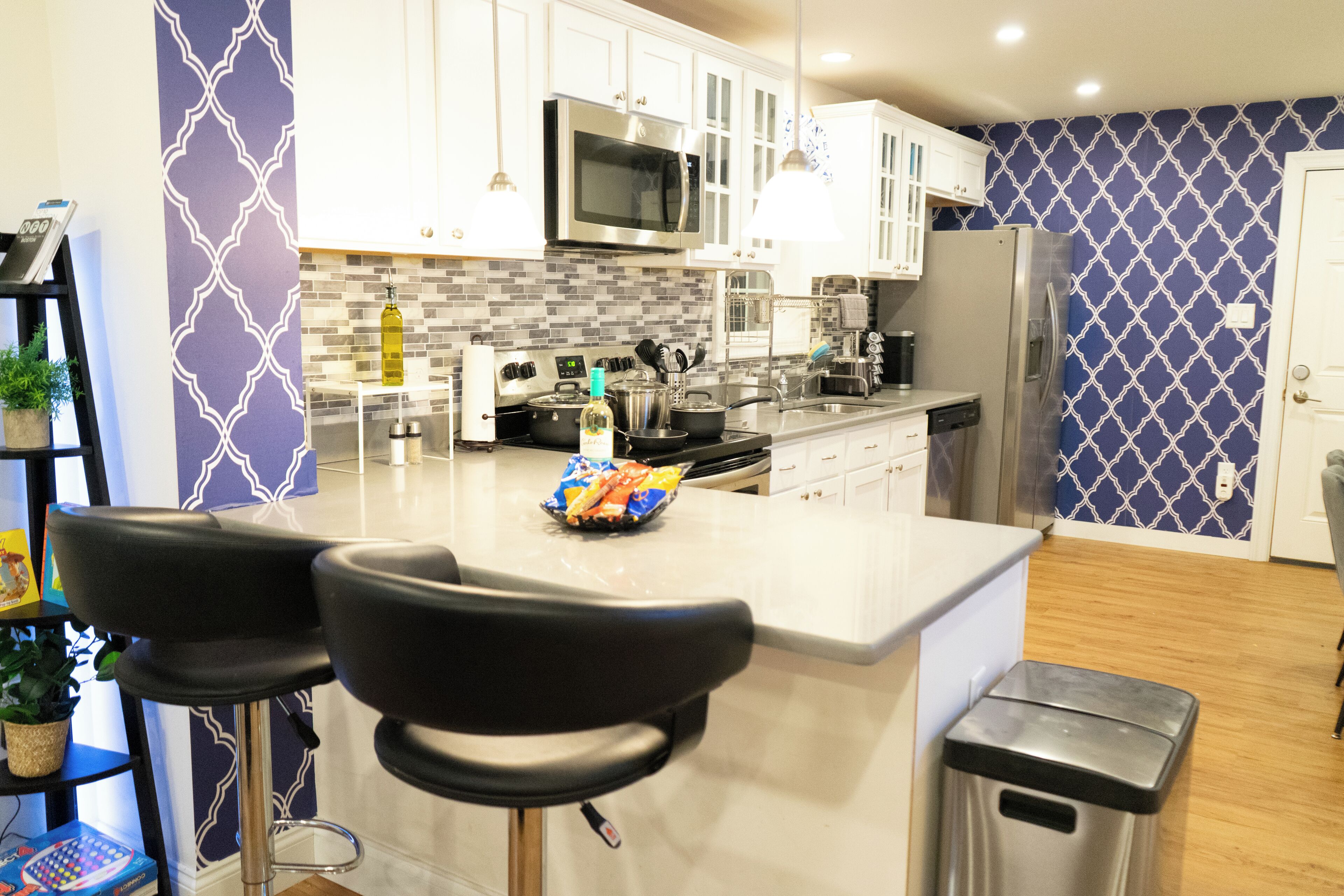 A modern kitchen with white cabinets, a stainless steel refrigerator, a microwave, and a central island with bar stools.