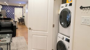 Un lavadero con lavadoras apiladas y una puerta que da a un área de estar con sofá y mesa de centro.