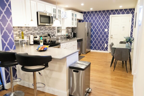 A modern kitchen with white cabinets, a stainless steel refrigerator, and a central island with bar stools.