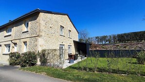 A stone building with a sloped roof, a front porch, and a small garden area.