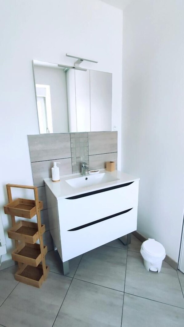 A modern bathroom with a white vanity, a wooden shelf, and a toilet.