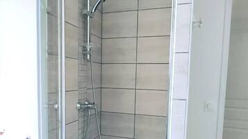 A glass-enclosed shower with a handheld showerhead and a wall-mounted faucet.