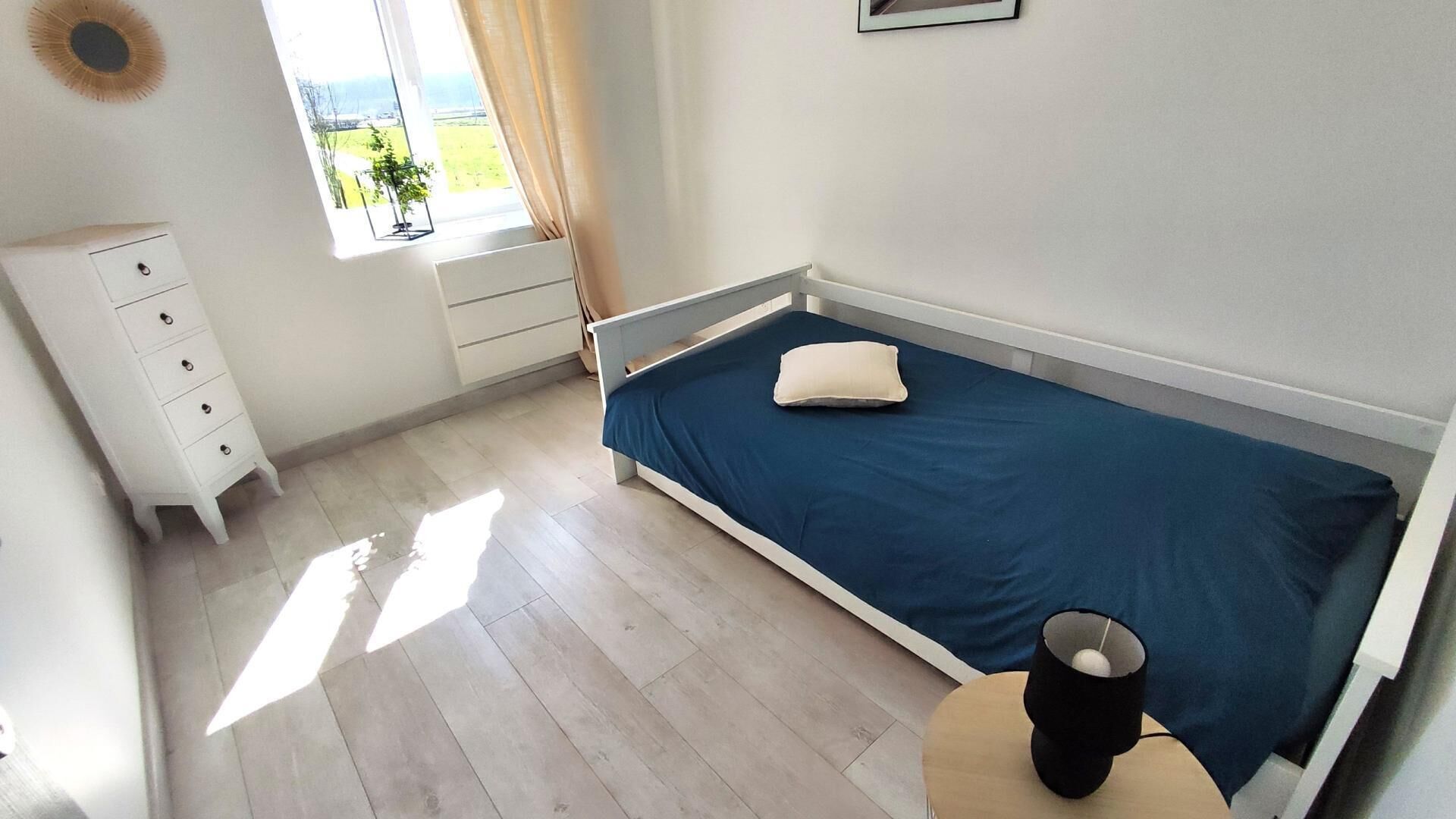 A bedroom with a single bed, a bedside table, a dresser, and a window with curtains.