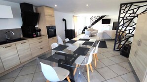 A modern kitchen with a dining area, featuring a glass table, white chairs, and a staircase leading to another level. - HEIDI - SURY - Gîte (SURY)