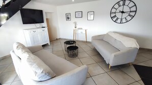 A living room with a sofa, a coffee table, a TV, a clock, and framed pictures on the wall. - HEIDI - SURY - Gîte (SURY)