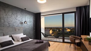 Une chambre moderne avec un grand lit, une vue sur la ville et un balcon équipé d’une chaise.