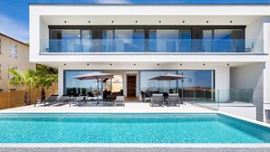 Une maison moderne à deux étages, dotée d’une piscine, d’un espace salon extérieur et de grandes baies vitrées.