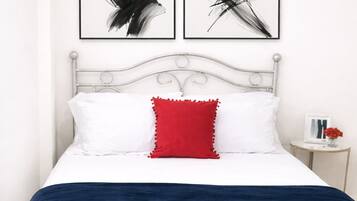A bed with white bedding, a red pillow, and two abstract art pieces above it.