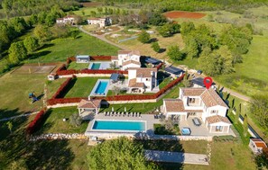 An aerial view of a residential area with multiple houses, a swimming pool, and a red location marker. - Amazing home in Jadruhi with sauna (Jadruhi)