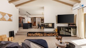 Ein modernes Wohnzimmer mit einer Couch, einem Couchtisch und einem Kamin. Es gibt einen Essbereich mit Tisch und Stühlen, und im Hintergrund eine Küche.