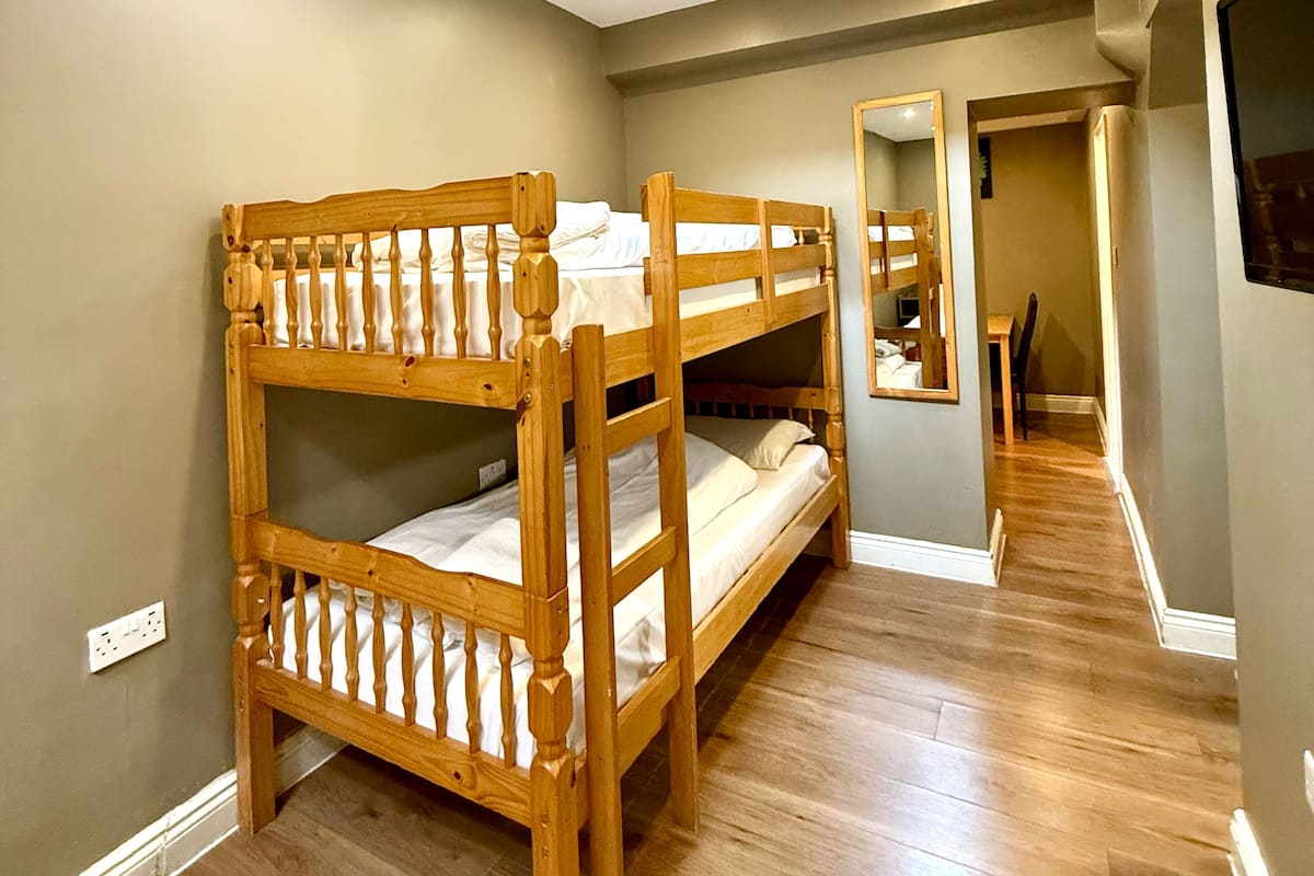 A room with bunk beds, a skylight, a wooden floor, and a hallway leading to another room.