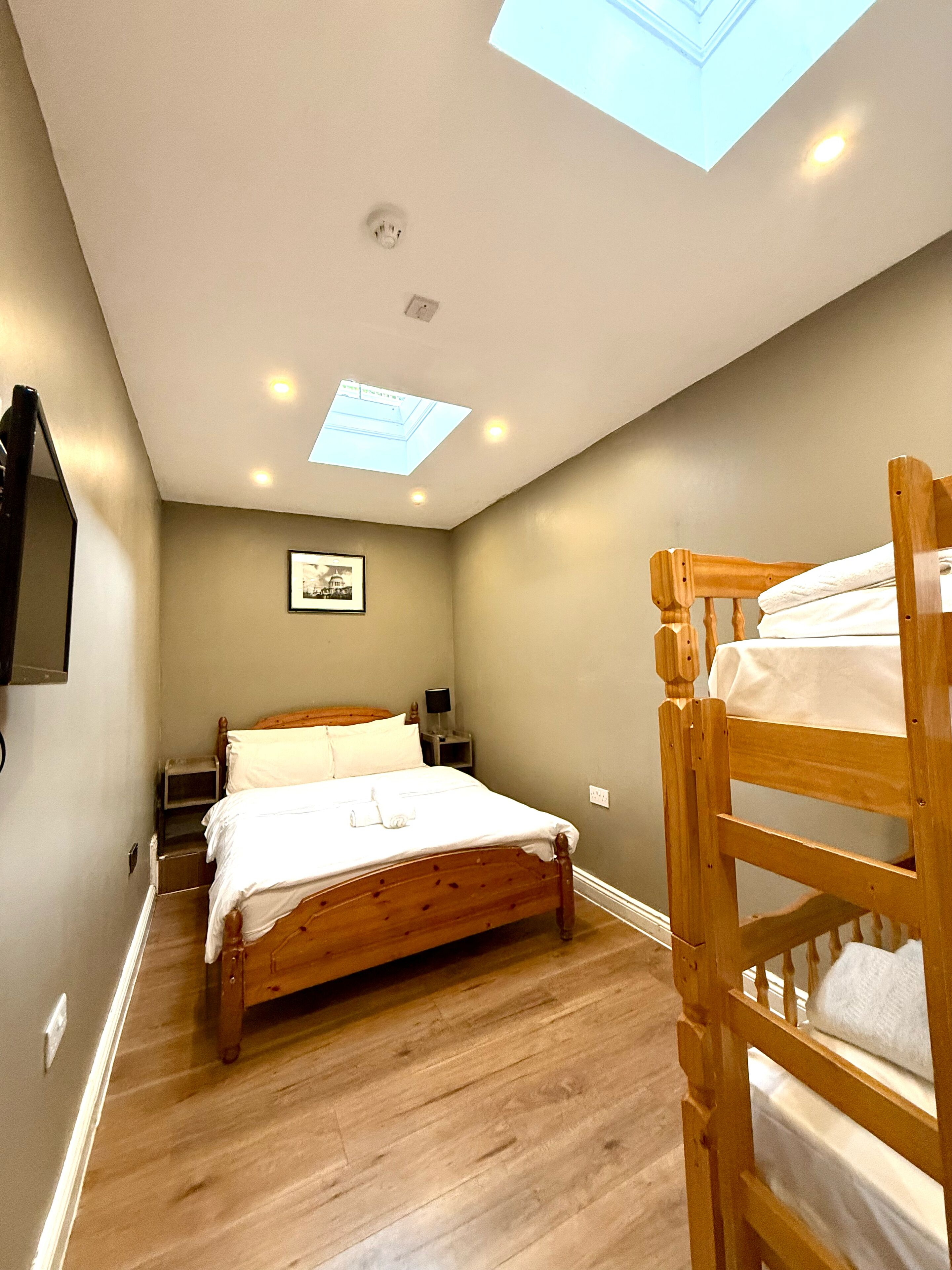 Un dormitorio con cama de madera, una mesita de noche, una lámpara de techo y un tragaluz.