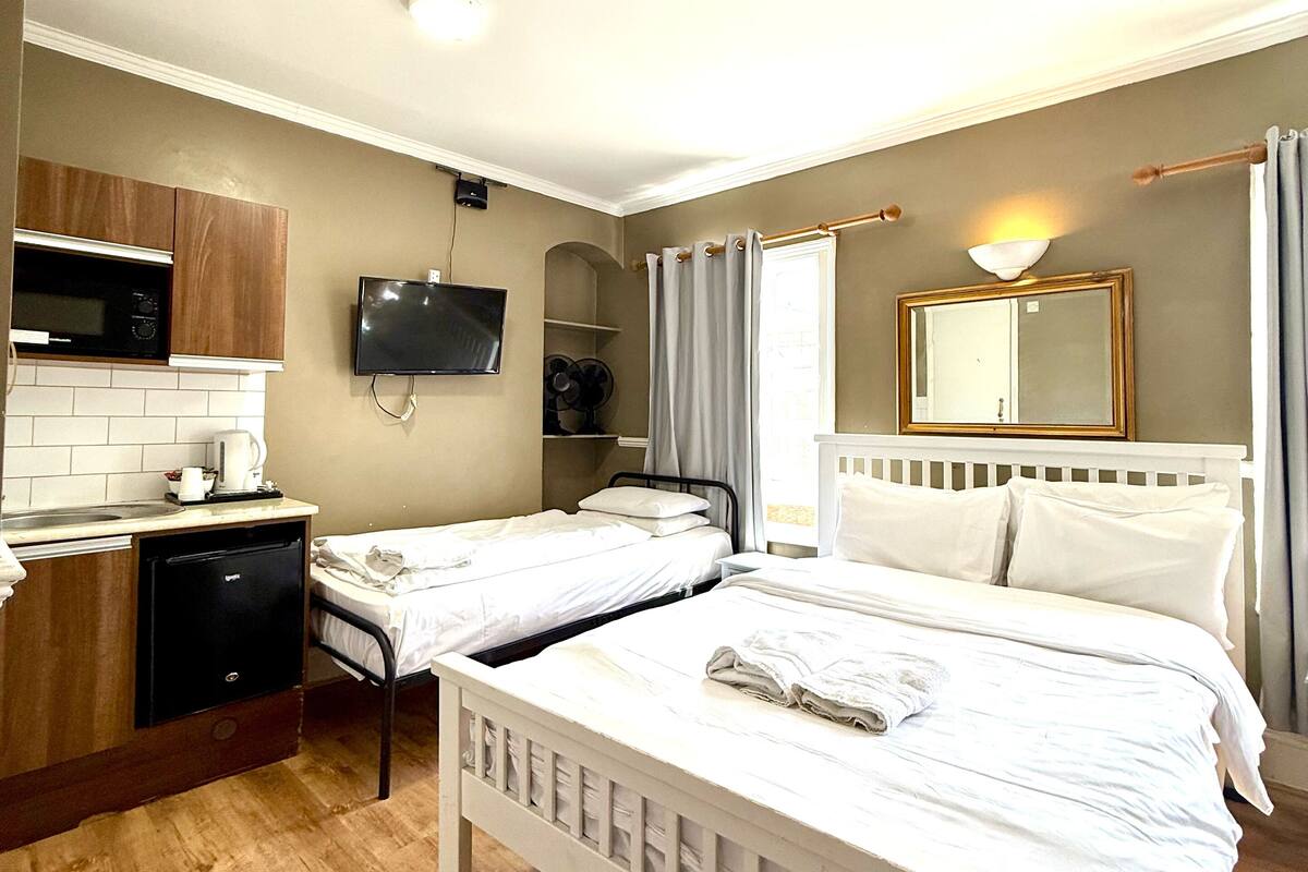 A hotel room with two single beds, a small kitchenette with a microwave, and a TV.