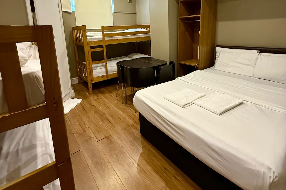 A hotel room with a bunk bed, a single bed, a desk, and a wardrobe.