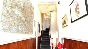 Un corridoio con una mappa, quadri incorniciati, una scala e un estintore.