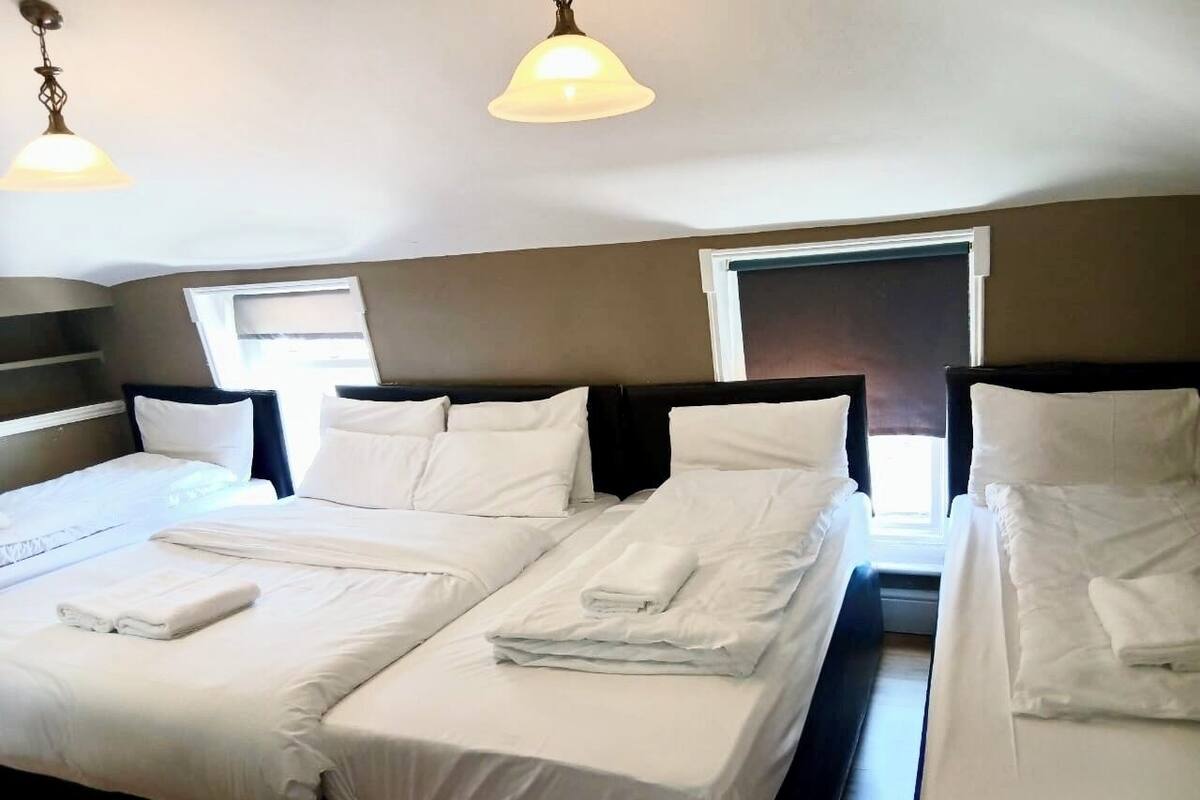 A hotel room with two beds, each with white linens and pillows, a large window, and a ceiling light fixture.