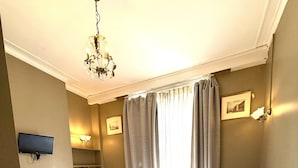 Una camera d'albergo con un letto, una televisione, un lampadario e una finestra con tende.