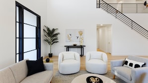 Un salon spacieux avec un haut plafond, un escalier et une grande fenêtre.
