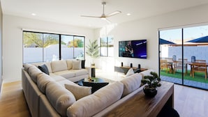 Un salon moderne avec un canapé d’angle, une table basse, un téléviseur et une vue sur l’extérieur.