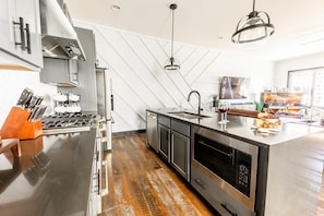 A modern kitchen with stainless steel appliances, a central island, and a herringbone-patterned wall.
