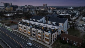 A modern multi-story building with a rooftop terrace, located in an urban area with surrounding high-rise buildings. - Broadway Getaway-rooftop Patio-mins to The Gulch (Nashville)