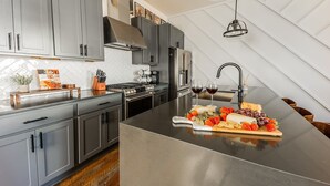 A modern kitchen with grey cabinets, stainless steel appliances, and a central island with a fruit and cheese platter. - Broadway Getaway-rooftop Patio-mins to The Gulch (Nashville)